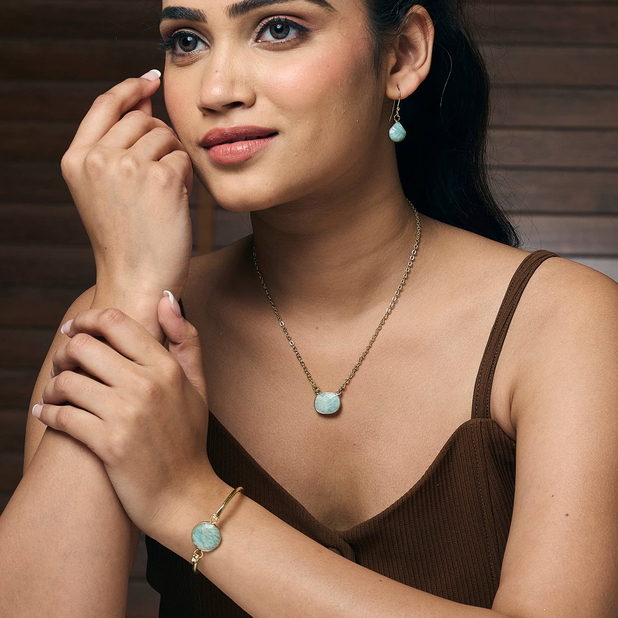 Woman wearing turquoise earrings and bracelet with a brown top against a wooden background