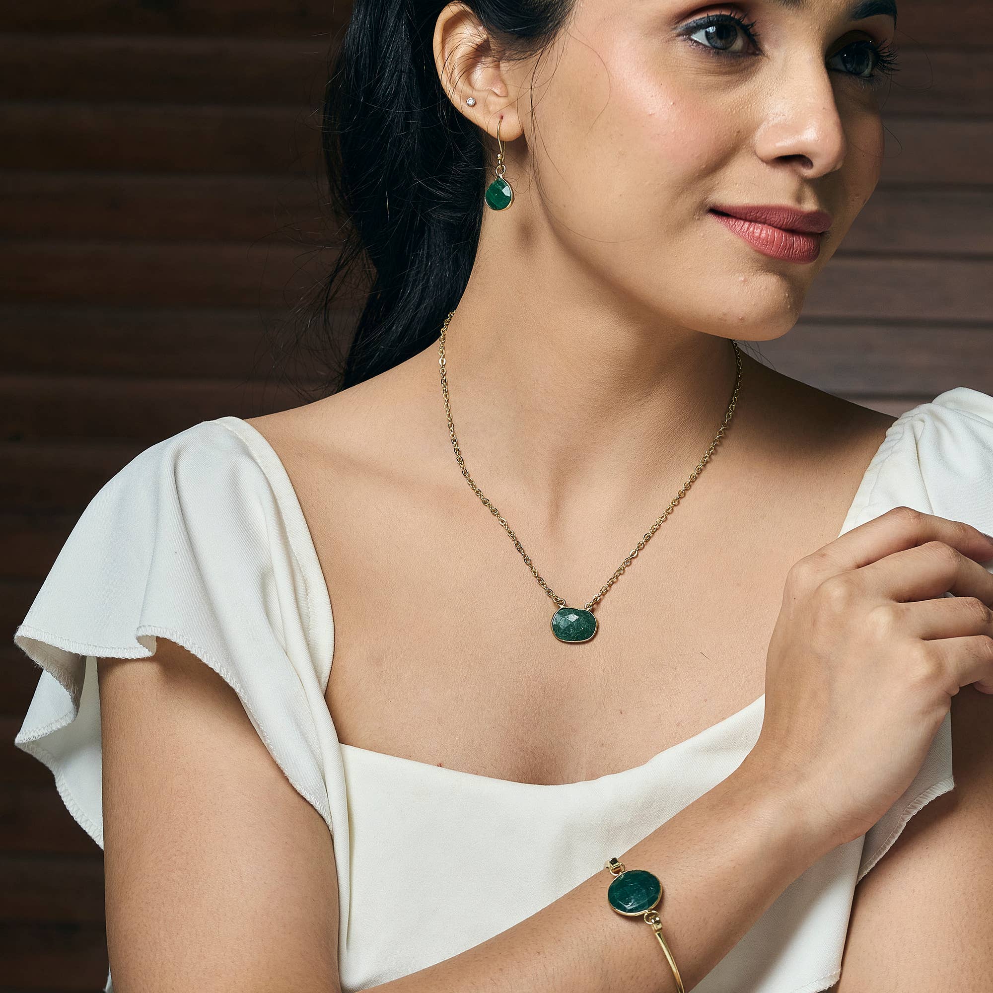 Woman wearing a necklace and bracelet with a green pendant against a wooden background