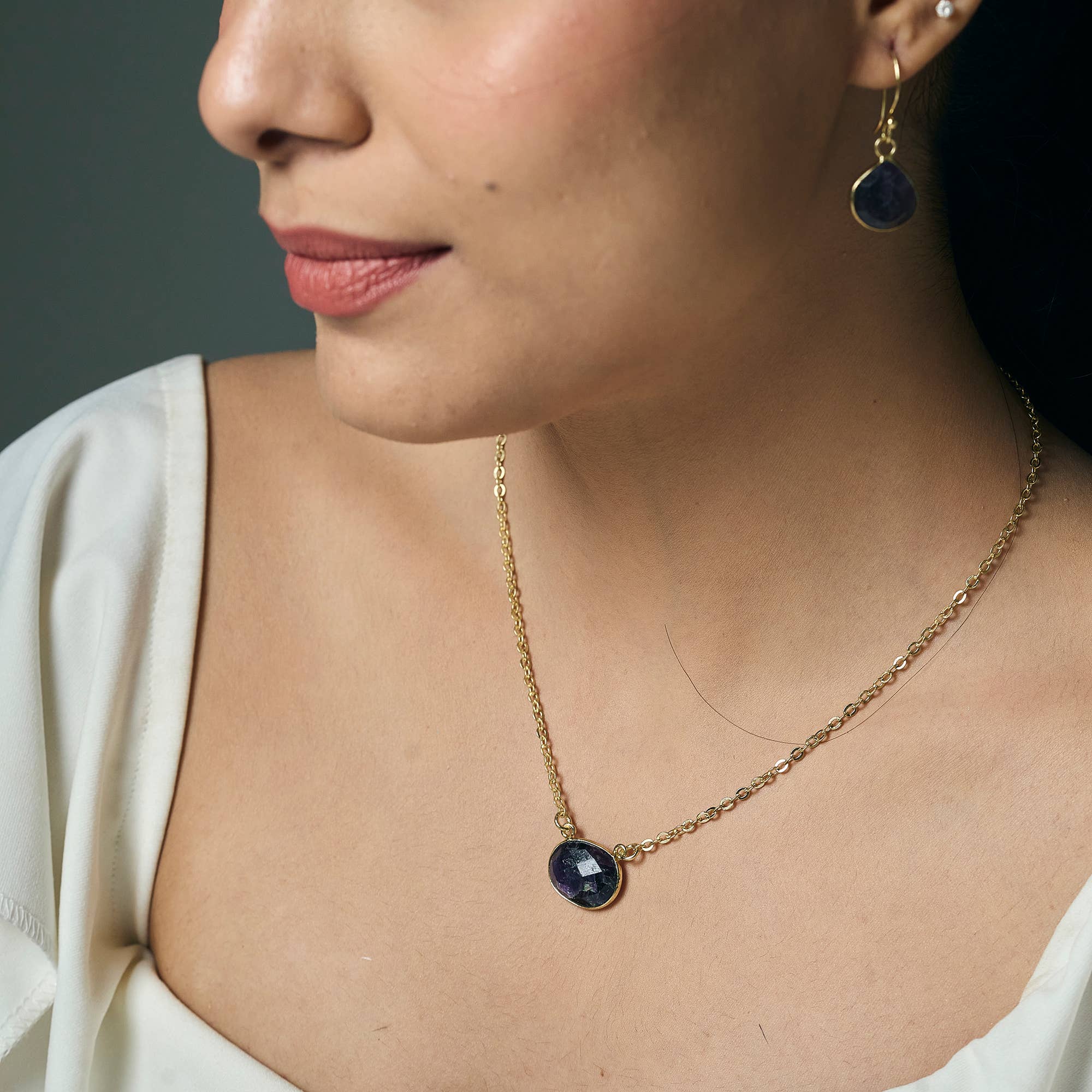 Close-up of a woman wearing a gold necklace with a blue gemstone pendant and matching earrings.