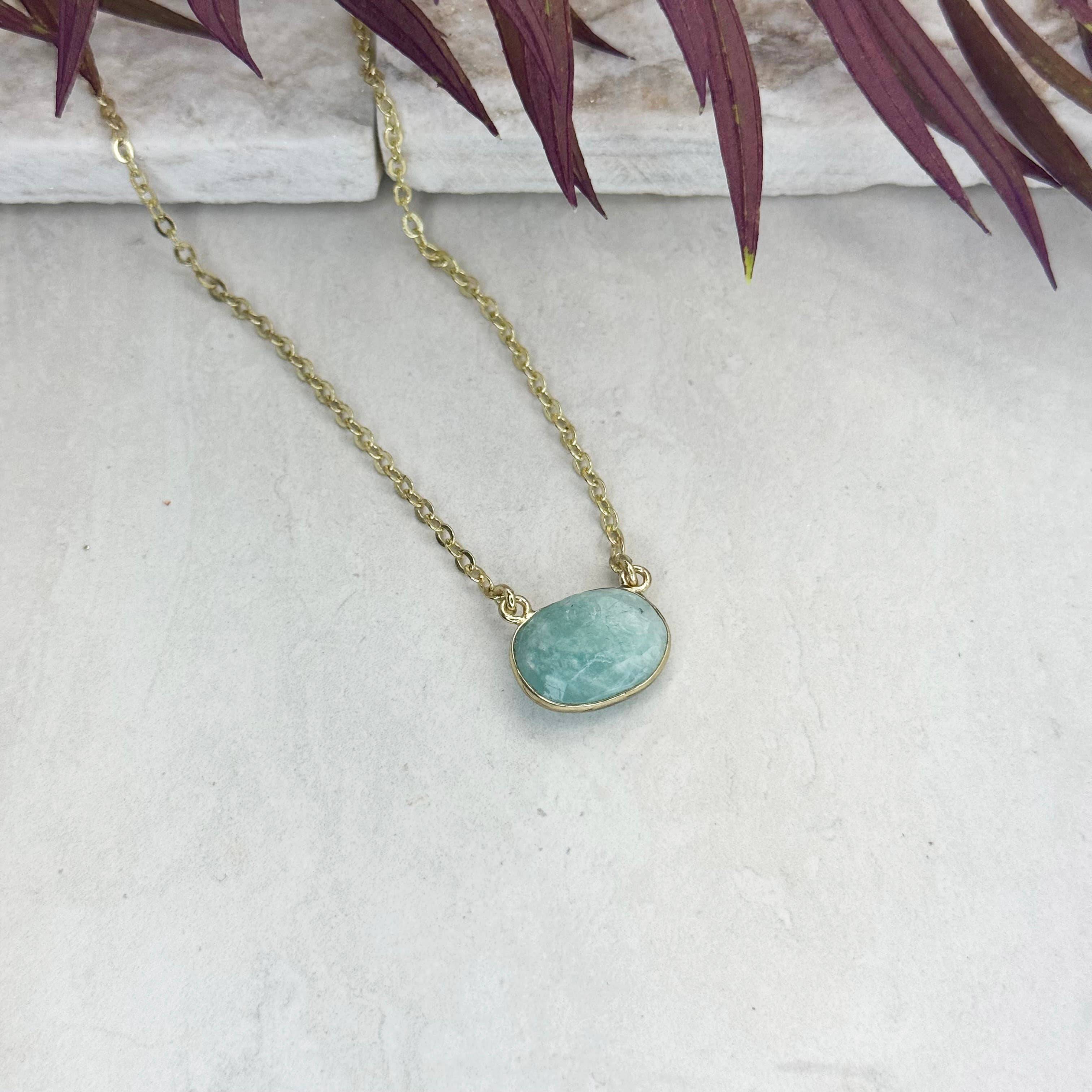 Necklace with a turquoise pendant on a light gray surface with purple leaves in the background