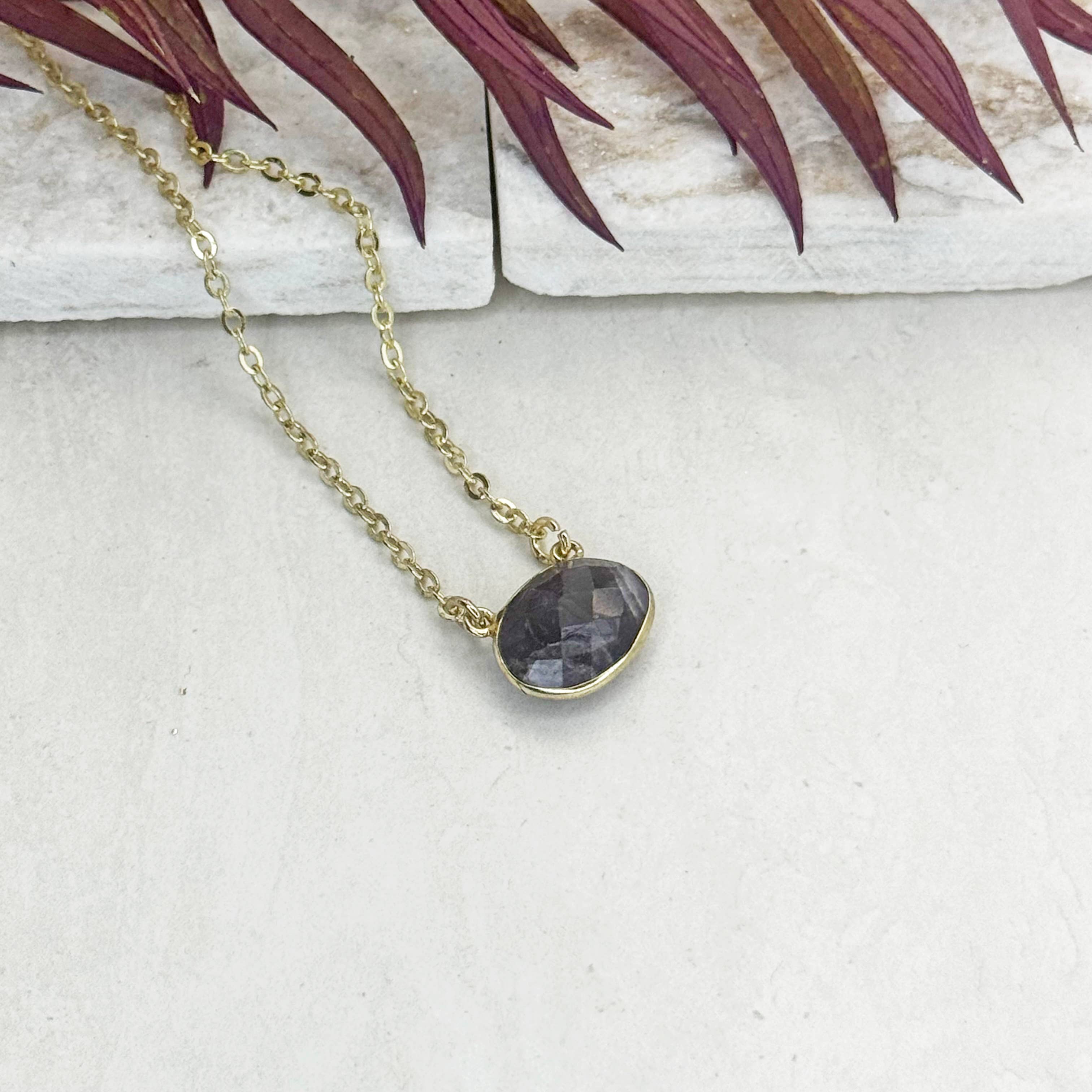 Necklace with a dark stone pendant on a textured surface with leaves in the background